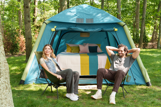 couple sitting in camping chairs outside of tent with bed made inside