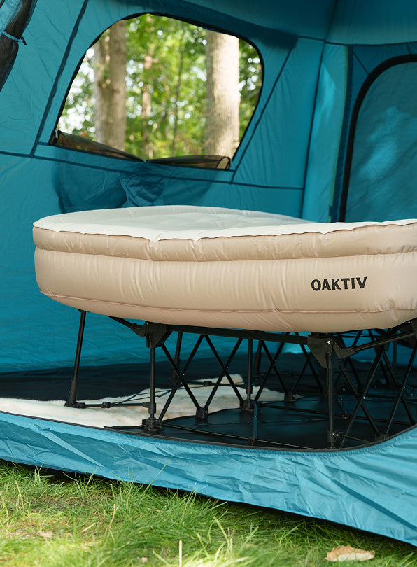 Camping bed with 'OAKTIV' branding inside a blue tent with trees in the background